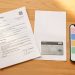 Dossier administratif de santé posé sur une table claire avec un document fiscal neutre, une carte d’assurance maladie sans marquage et un téléphone affichant une interface abstraite.