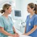 Femme adulte dans une salle de radiologie lumineuse, échangeant un regard rassurant avec une manipulatrice avant un examen de mammographie.
